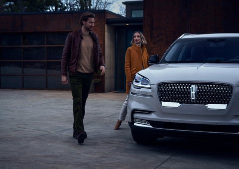 A man and a woman approaching a 2024 Lincoln Aviator® SUV, which illuminates certain lights when they are close | Magic City Lincoln in Roanoke VA