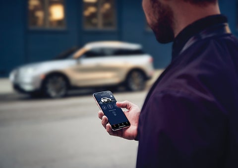 A person is shown interacting with a smartphone to connect to a Lincoln vehicle across the street. | Magic City Lincoln in Roanoke VA