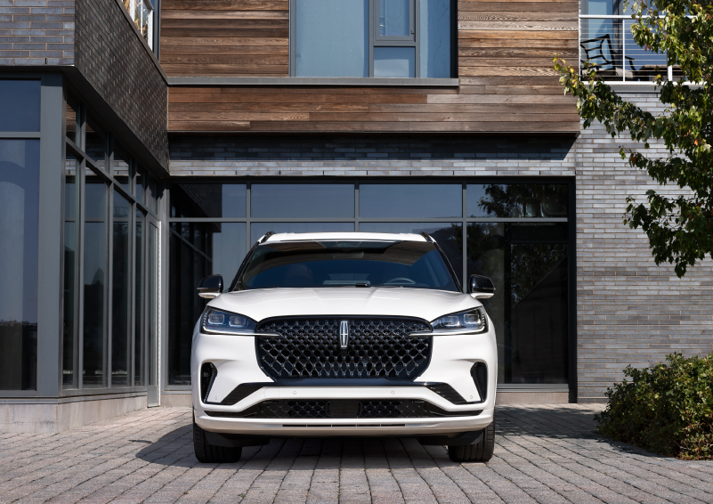A white 2025 Lincoln Aviator® SUV is shown parked outside a modern building with gray brick and wood accents. | Magic City Lincoln in Roanoke VA
