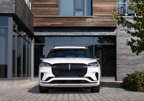 A white 2025 Lincoln Aviator® SUV is shown parked outside a modern building with gray brick and wood accents. | Magic City Lincoln in Roanoke VA