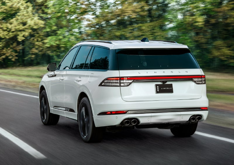 A white 2026 Lincoln Aviator® SUV is being driven away down a road lined with colorful trees. | Magic City Lincoln in Roanoke VA