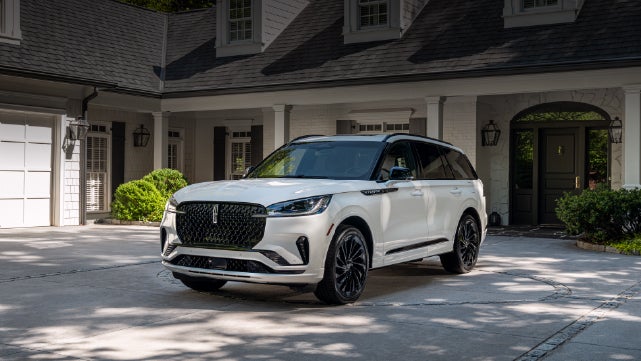 A white 2026 Lincoln Aviator® SUV is parked in the driveway of a luxury home. | Magic City Lincoln in Roanoke VA