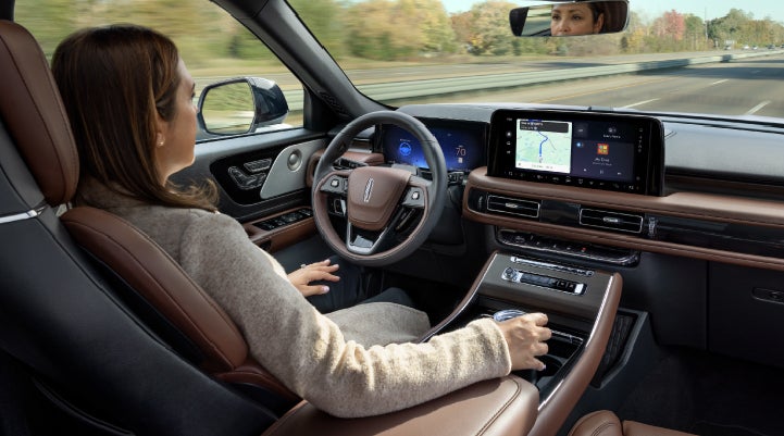 A 2027 Lincoln Aviator® SUV is being driven hands-free on a highway lined with trees. | Magic City Lincoln in Roanoke VA