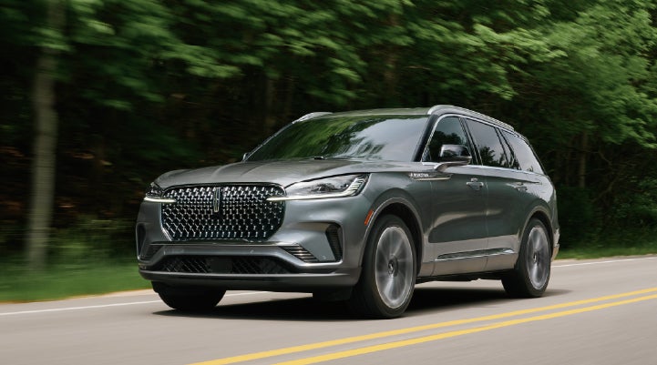 A 2027 Lincoln Aviator® SUV is being driven down a road lined with trees. | Magic City Lincoln in Roanoke VA